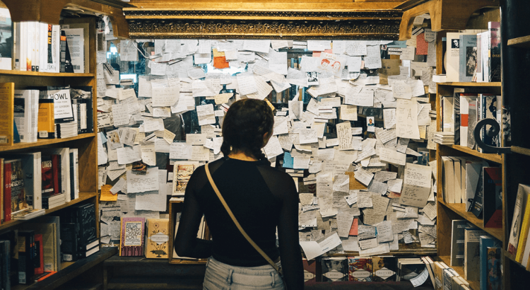 Dziewczyna w księgarni stoi przed tablicą z mnóstwem zapisanych karteczek.