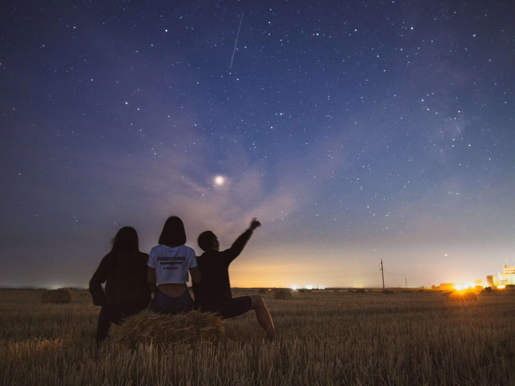 trzy osoby siedzące na polu oglądające spadające gwiazdy